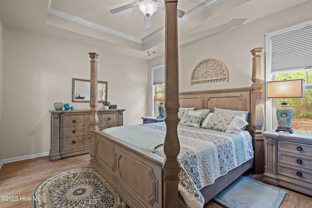 bedroom featuring a tray ceiling, crown molding, light wood finished floors, ceiling fan, and ornate columns