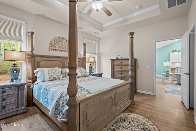 bedroom featuring light wood-type flooring, visible vents, ornamental molding, a raised ceiling, and ornate columns