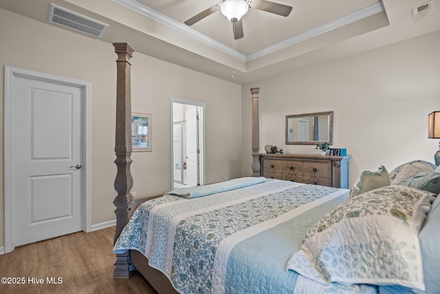 bedroom featuring a raised ceiling, wood finished floors, visible vents, and ornate columns