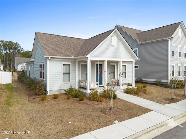 view of front of property with covered porch, a shingled roof, and fence