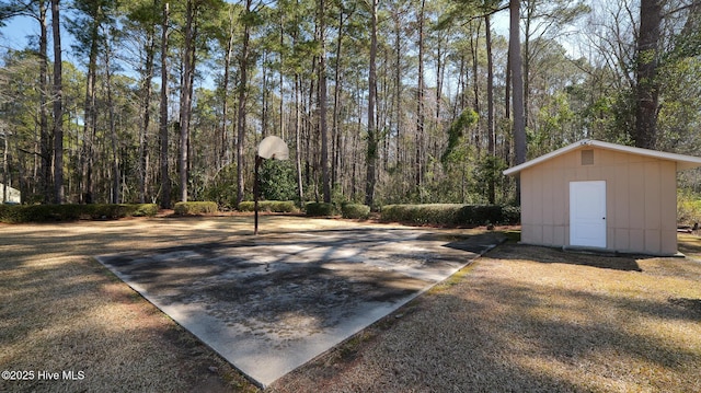 view of patio with a view of trees, an outdoor structure, basketball hoop, and a shed