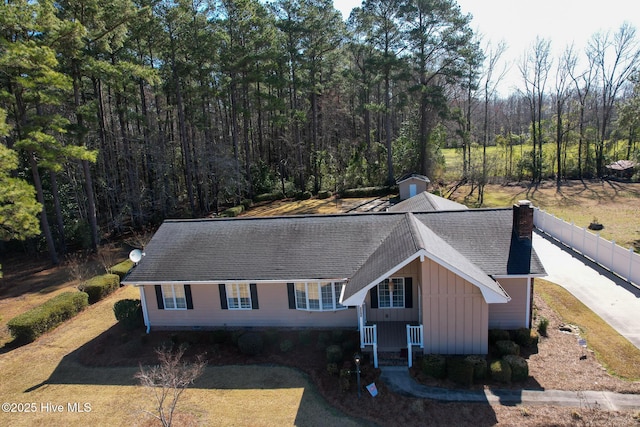 view of front of house featuring fence, board and batten siding, a wooded view, an outdoor structure, and a chimney