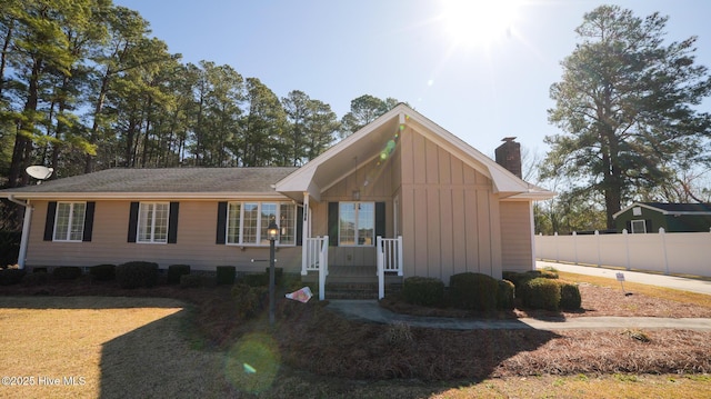 view of front of property featuring board and batten siding, a chimney, and fence