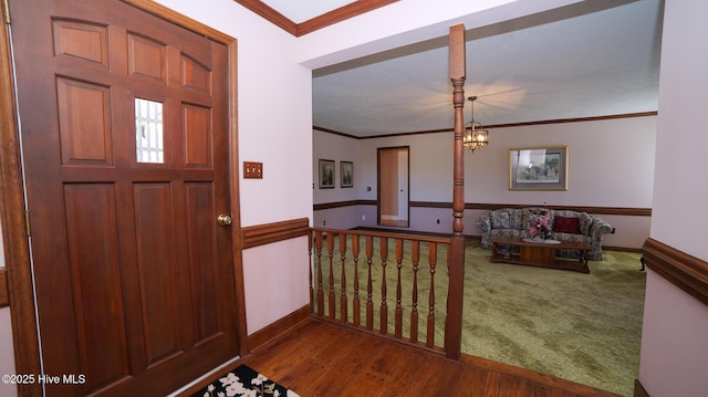 carpeted entrance foyer with baseboards, an inviting chandelier, wood finished floors, and crown molding