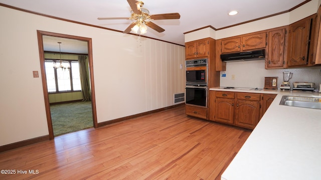 kitchen with under cabinet range hood, light countertops, dobule oven black, and ornamental molding