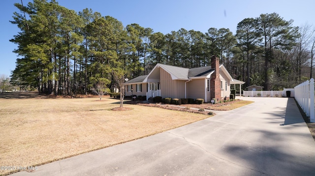 view of property exterior featuring fence, board and batten siding, driveway, and a chimney