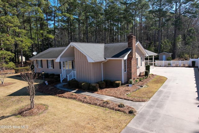 view of front facade with board and batten siding, a front lawn, fence, concrete driveway, and a chimney