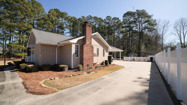 view of side of property featuring fence, roof with shingles, driveway, a chimney, and board and batten siding