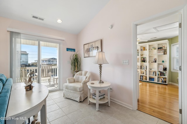 living area featuring visible vents, baseboards, attic access, vaulted ceiling, and light tile patterned flooring