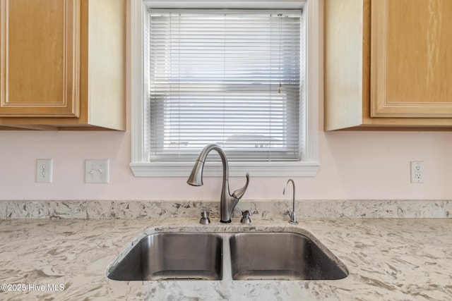 kitchen featuring light stone countertops, light brown cabinetry, and a sink