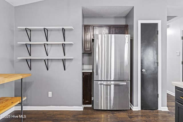 kitchen with dark wood-type flooring, freestanding refrigerator, dark brown cabinetry, light countertops, and baseboards