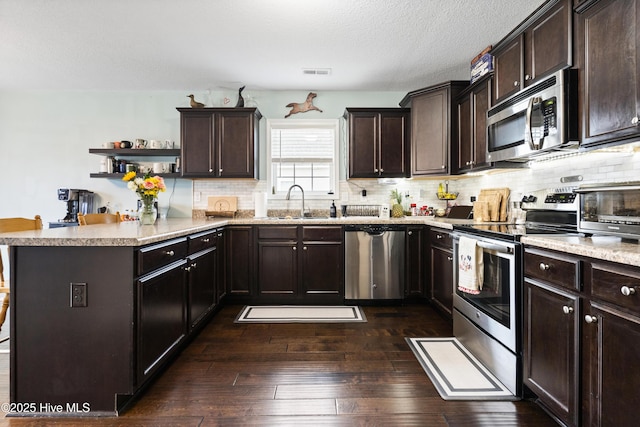 kitchen with visible vents, dark wood finished floors, stainless steel appliances, dark brown cabinetry, and a peninsula