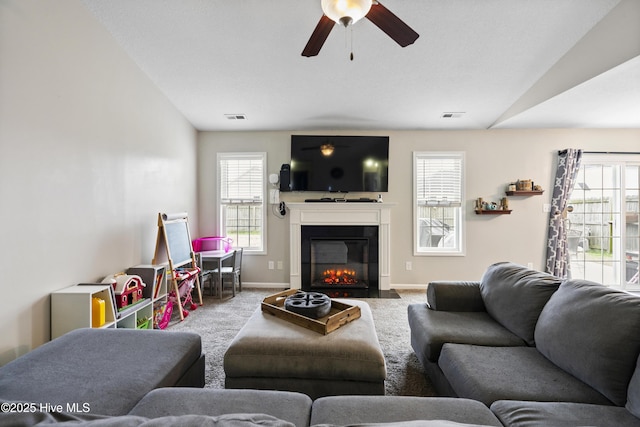 carpeted living area featuring visible vents, a fireplace with flush hearth, a ceiling fan, and baseboards