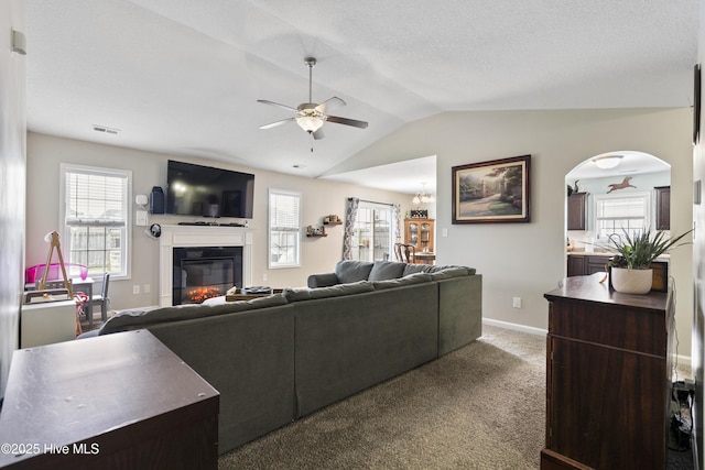 living area with visible vents, vaulted ceiling, carpet floors, a glass covered fireplace, and a ceiling fan
