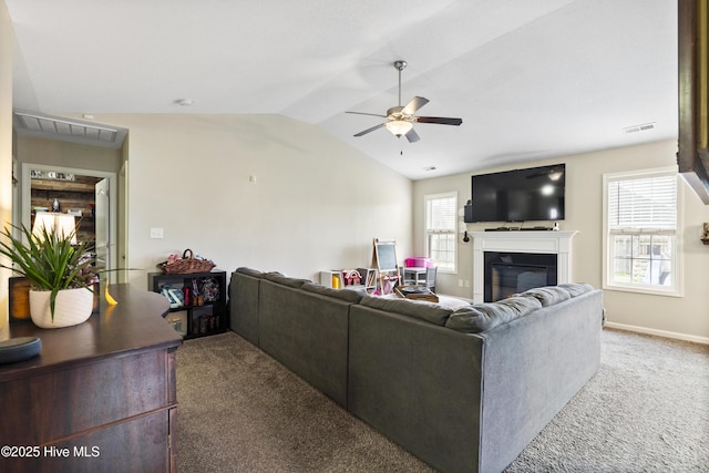 carpeted living area with visible vents, baseboards, vaulted ceiling, a glass covered fireplace, and a ceiling fan