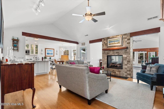 living area featuring visible vents, track lighting, ceiling fan, light wood-type flooring, and a stone fireplace