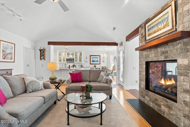 living room with visible vents, ceiling fan with notable chandelier, a glass covered fireplace, light wood-style floors, and lofted ceiling