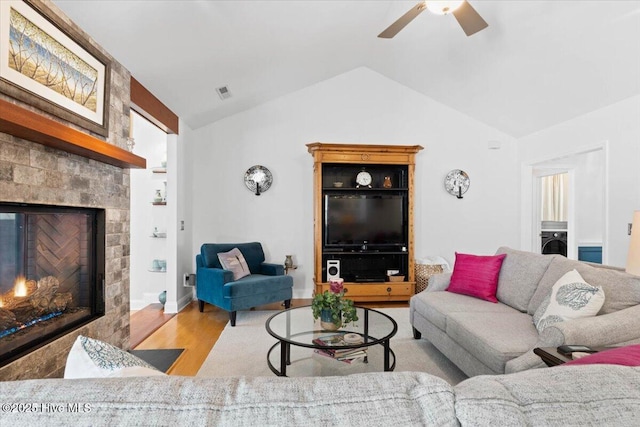 living area with visible vents, a ceiling fan, a glass covered fireplace, wood finished floors, and lofted ceiling