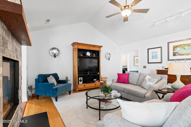 living area featuring visible vents, lofted ceiling, a fireplace, wood finished floors, and a ceiling fan