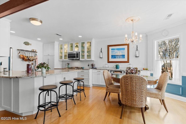 dining space with light wood finished floors, visible vents, a chandelier, and ornamental molding