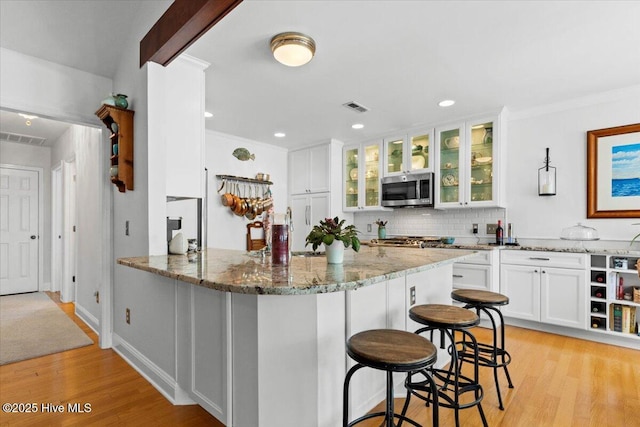 kitchen with stainless steel microwave, a breakfast bar area, light wood-style floors, and visible vents