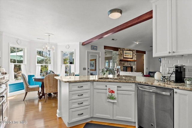 kitchen featuring a sink, a peninsula, white cabinets, a stone fireplace, and dishwasher