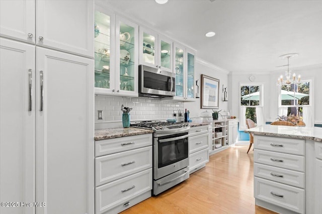 kitchen with light wood-style flooring, stainless steel appliances, white cabinetry, crown molding, and backsplash