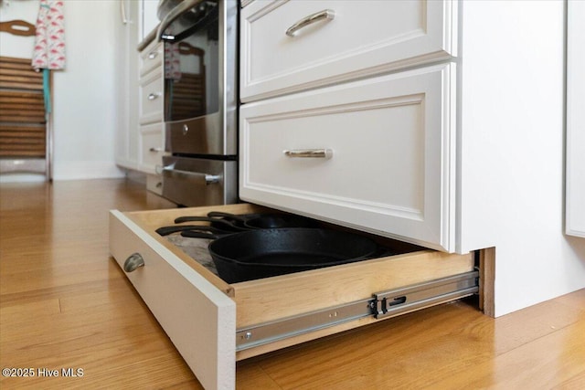 details with wall oven, white cabinets, and light wood-style floors