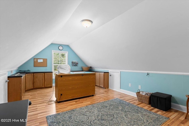 interior space featuring baseboards, light wood-style floors, and vaulted ceiling