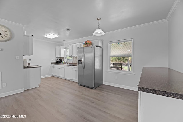 kitchen with ornamental molding, dark countertops, white cabinets, stainless steel fridge with ice dispenser, and dishwasher