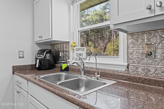 kitchen with dark countertops, white cabinetry, and a sink