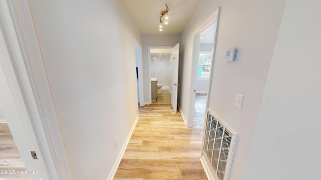 corridor featuring light wood-type flooring, visible vents, baseboards, and track lighting