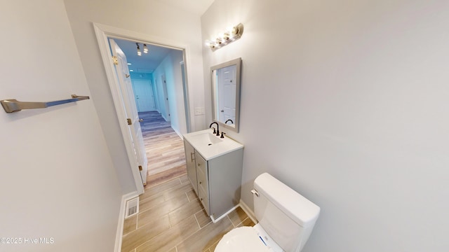 bathroom featuring vanity, baseboards, visible vents, wood finish floors, and toilet