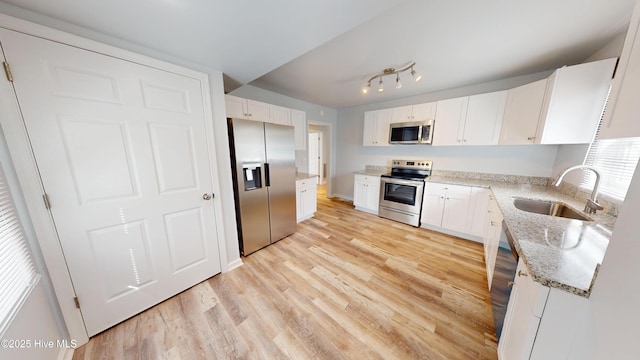 kitchen with light stone countertops, light wood-style flooring, a sink, white cabinets, and appliances with stainless steel finishes