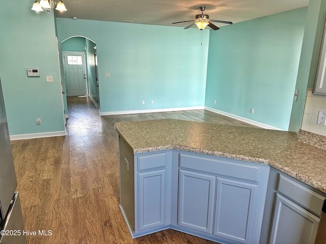 kitchen with a ceiling fan, baseboards, open floor plan, dark wood-type flooring, and arched walkways