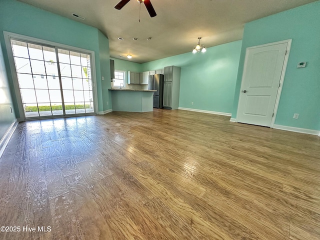 unfurnished living room featuring visible vents, baseboards, ceiling fan, and wood finished floors