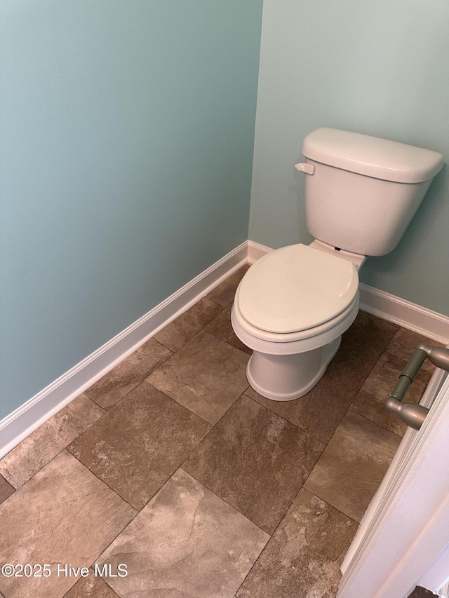 bathroom featuring baseboards, stone finish floor, and toilet