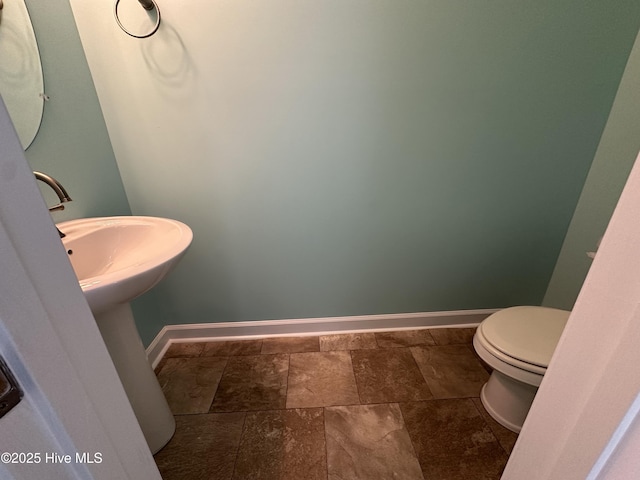 bathroom featuring stone tile floors, toilet, and baseboards