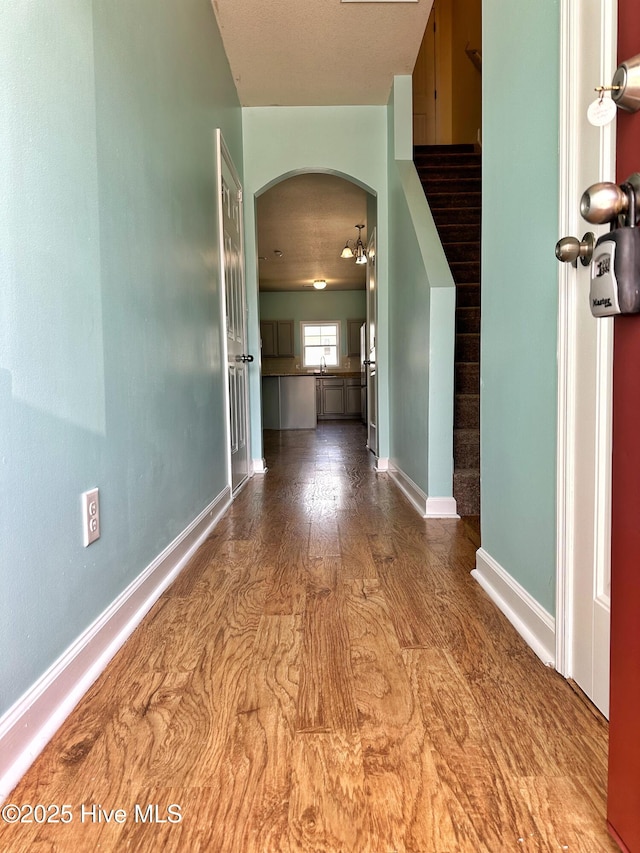hallway featuring arched walkways, baseboards, and wood finished floors