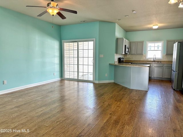 kitchen with a ceiling fan, appliances with stainless steel finishes, dark wood finished floors, a sink, and a peninsula