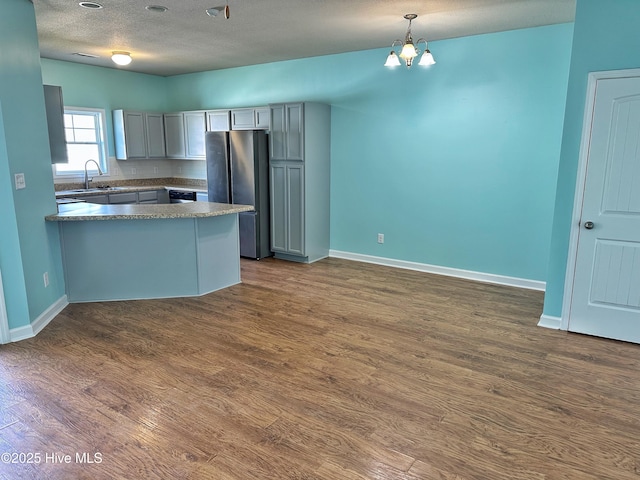 kitchen with a sink, freestanding refrigerator, a peninsula, and dark wood-style floors