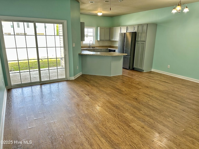 kitchen with dark wood-style flooring, a sink, freestanding refrigerator, a peninsula, and baseboards