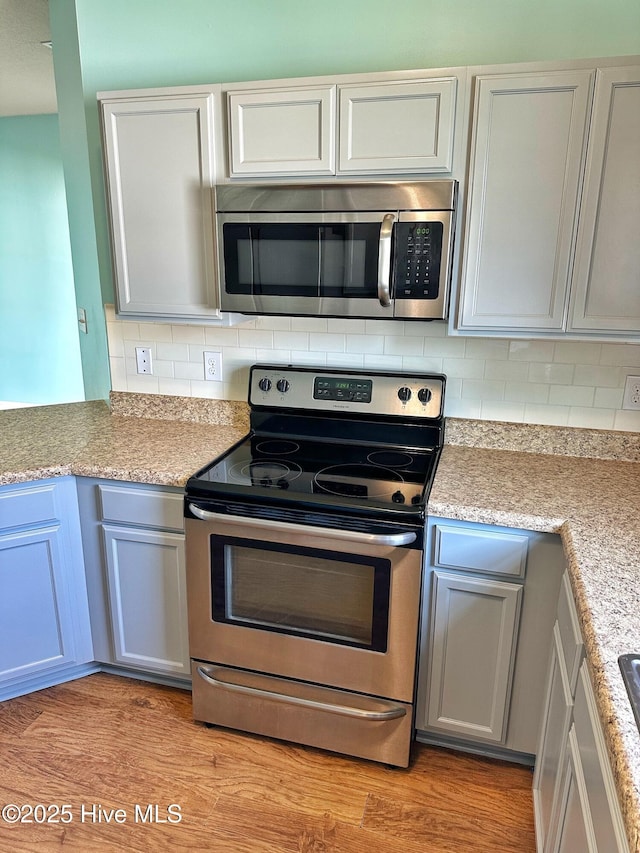 kitchen featuring light countertops, light wood-style flooring, appliances with stainless steel finishes, and backsplash