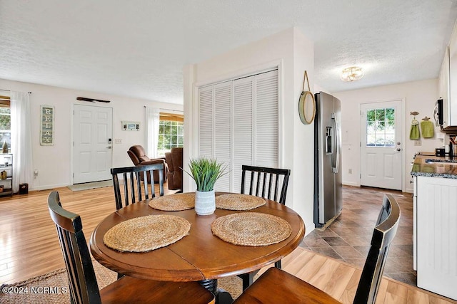 dining area featuring light wood-style flooring, a healthy amount of sunlight, baseboards, and a textured ceiling