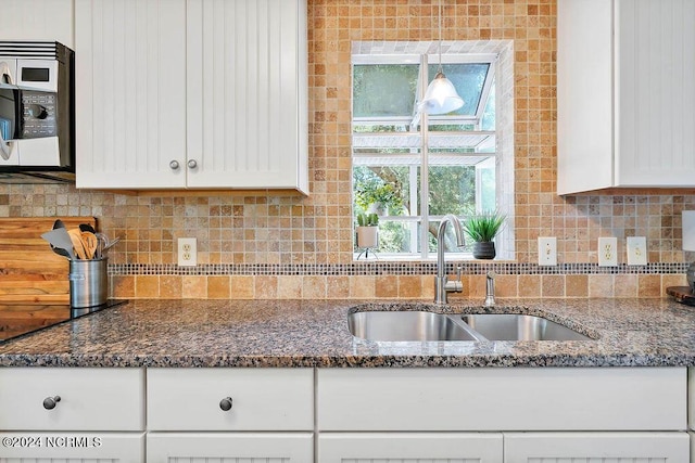 kitchen with stainless steel microwave, backsplash, white cabinetry, and a sink