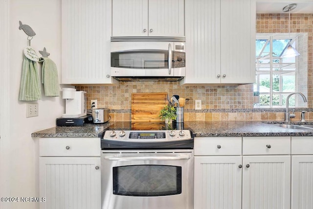 kitchen featuring decorative backsplash, dark stone countertops, appliances with stainless steel finishes, white cabinets, and a sink