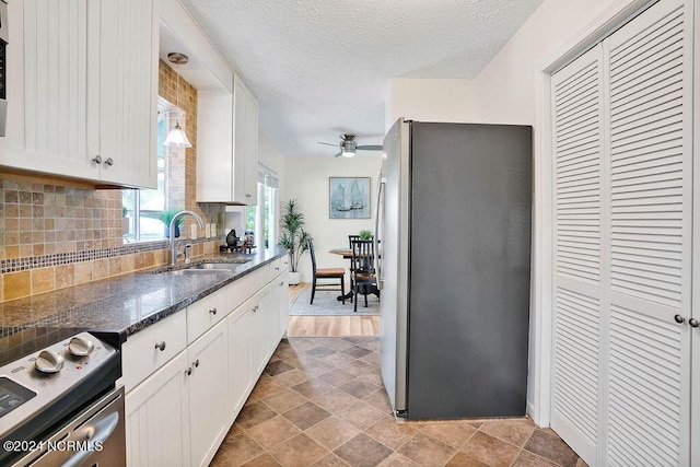 kitchen featuring dark stone counters, a sink, stainless steel appliances, white cabinets, and backsplash