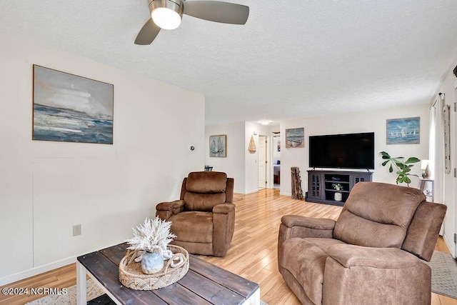 living area with baseboards, a textured ceiling, a ceiling fan, and light wood finished floors