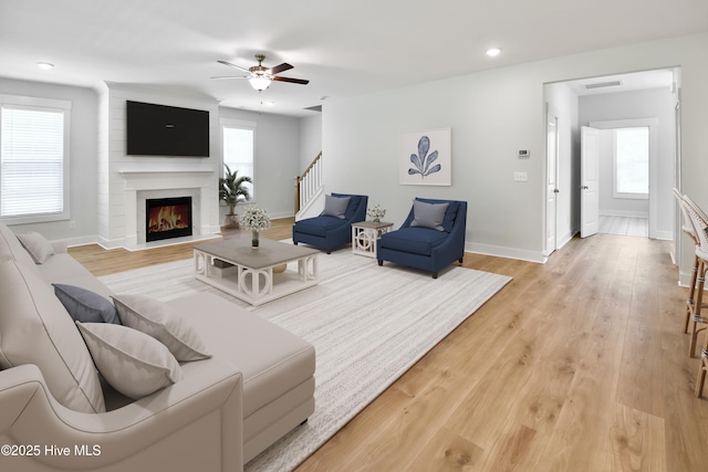 living area with visible vents, a fireplace, light wood finished floors, baseboards, and stairs