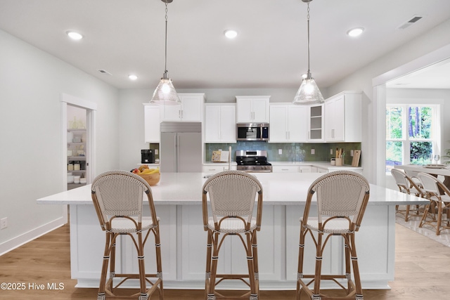 kitchen with decorative backsplash, light countertops, light wood-style floors, and appliances with stainless steel finishes